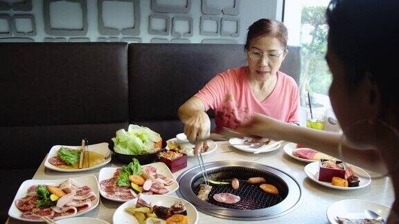 快乐的亚洲女人在热煤炉上烧烤猪肉韩式或日式烧烤