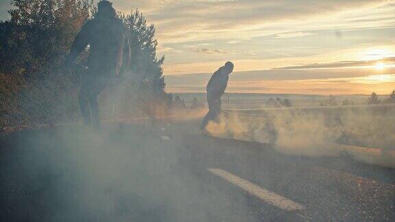 年轻人骑着滑板和烟雾弹在日落的道路上