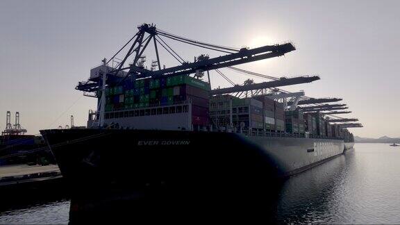 逆光拍摄货轮停靠港口塔吊货车装卸集装箱