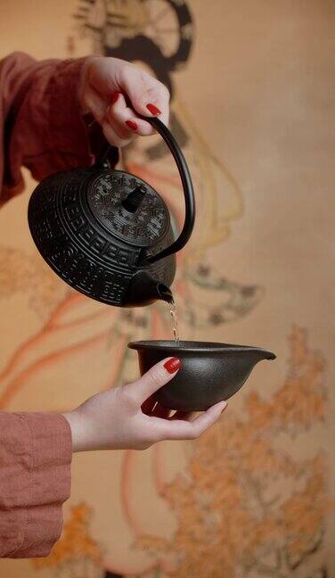 一个女人手提紫砂壶往茶盏里倒茶